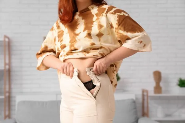 Image of woman trying to do her trousers up after pregnancy weight gain Oxfordshire
